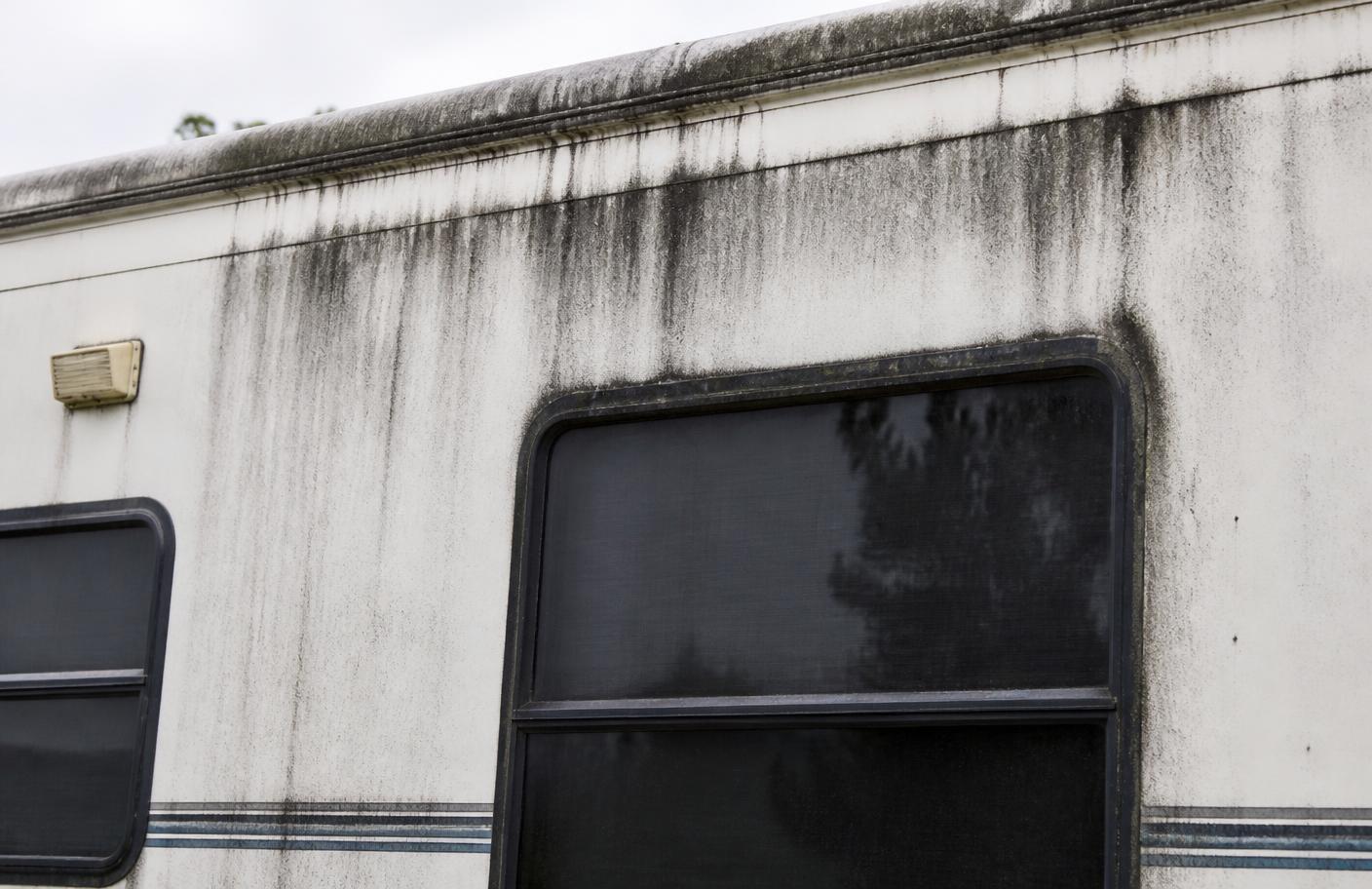 Black streak staining running down the sidewall and around a window frame of a dirty white RV